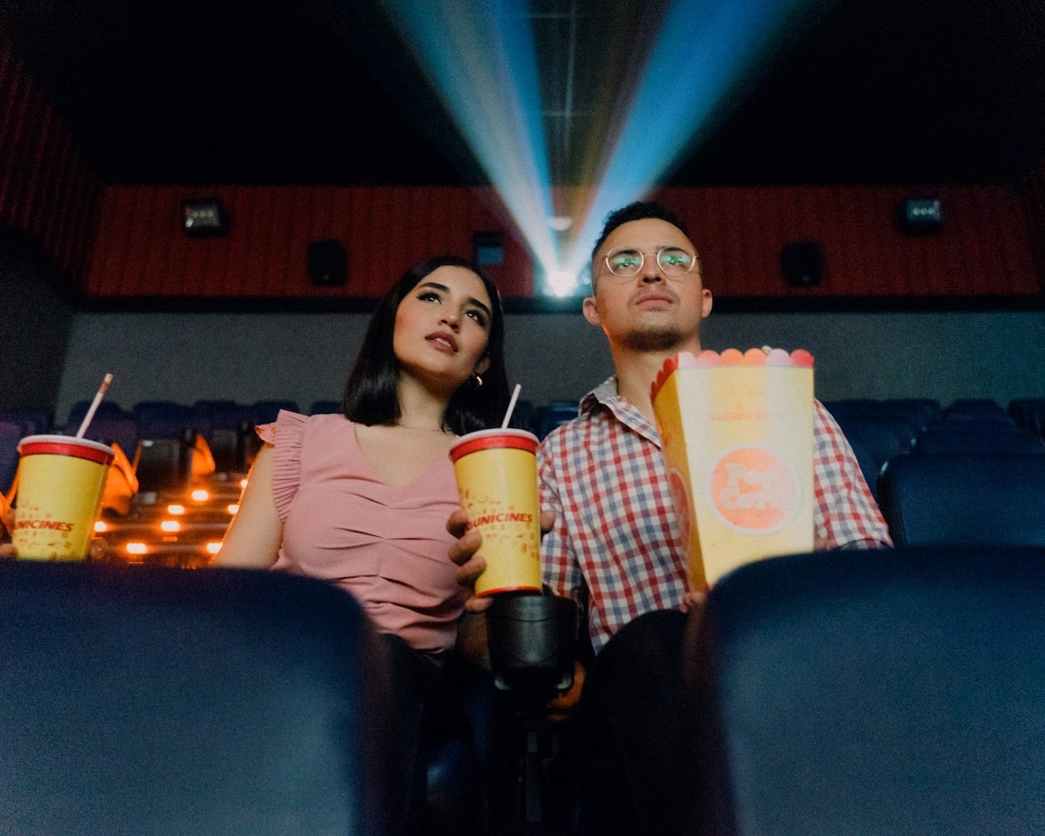 Box office 2024 2 women sitting on blue leather chair holding white and red plastic cups